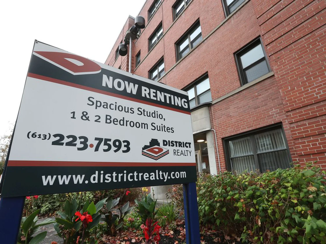 "Now Renting" sign outside of a 4 storey apartment building